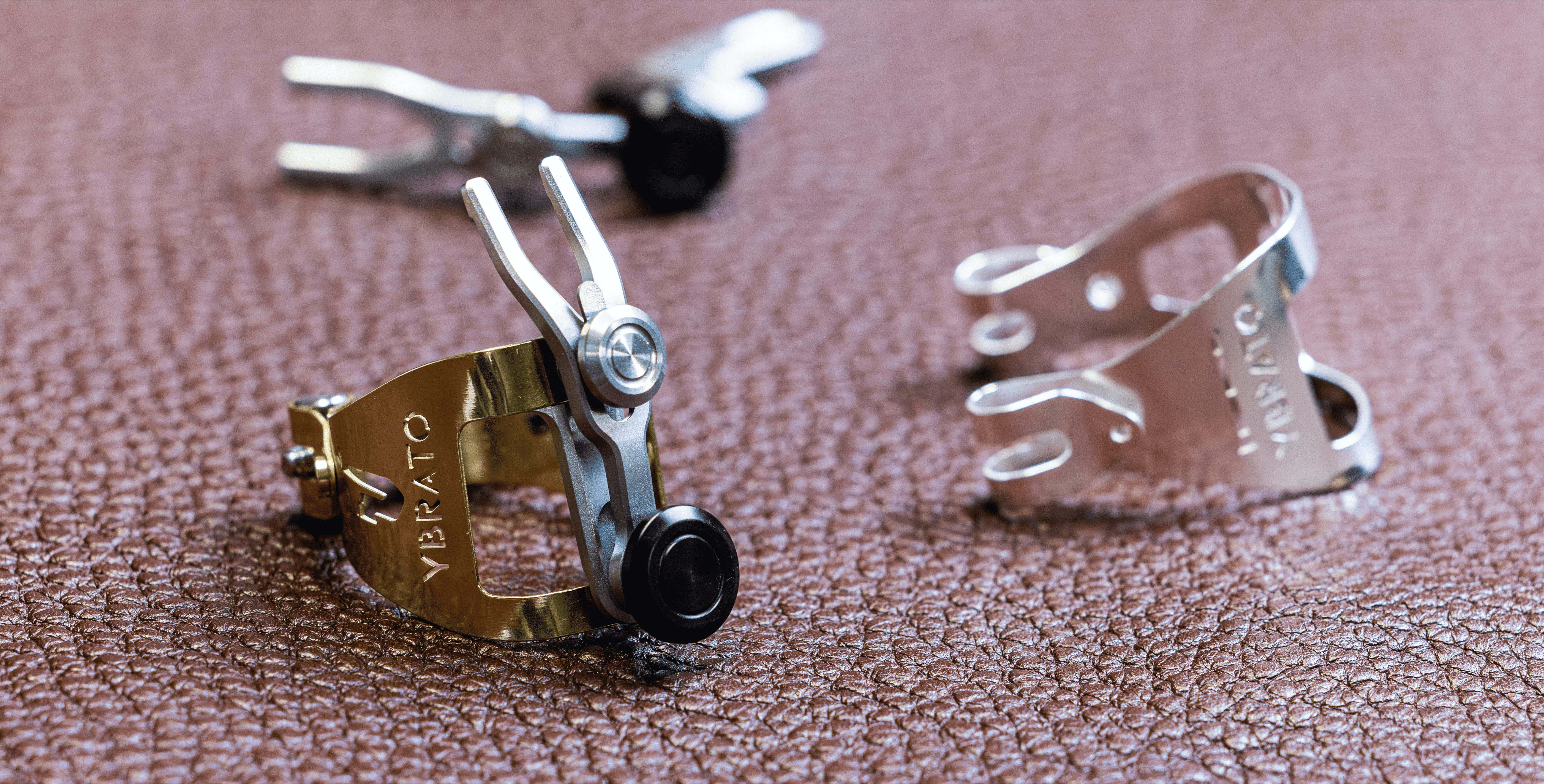 Showcase of gold and silver Ybrato saxophone ligatures on leather, demonstrating the different high-quality finishes and precision engineering of the SweetSpot series.