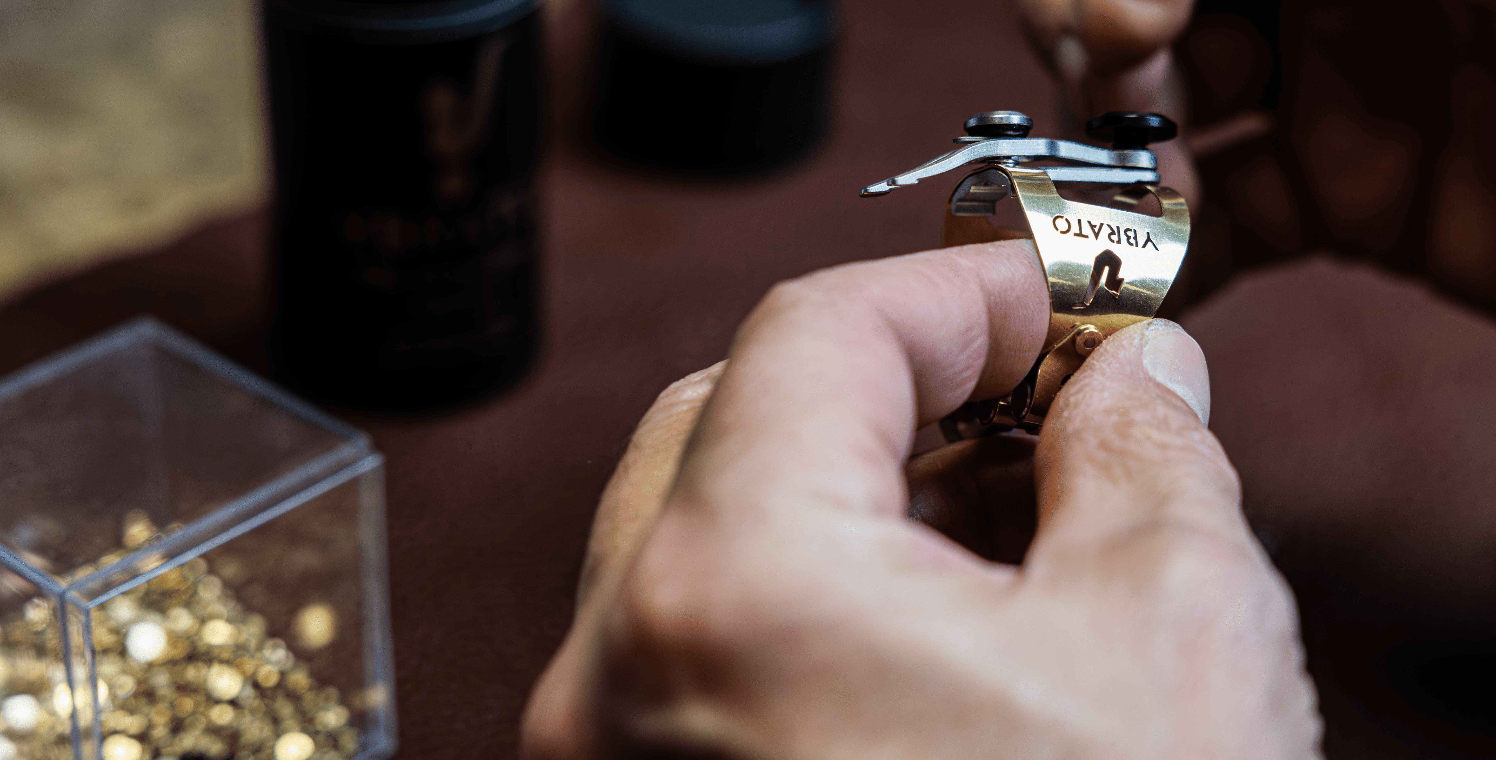 Close-up of the Ybrato SweetSpot Ligature being held by hand during the final assembly and manufacturing process, showcasing the detailed gold craftsmanship.